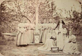 Retrato de un grupo de alumnas de uniforme con una religiosa en un jardín, unas bailando con lazos alrededor de una columna y otras cosiendo. Fotógrafo desconocido.